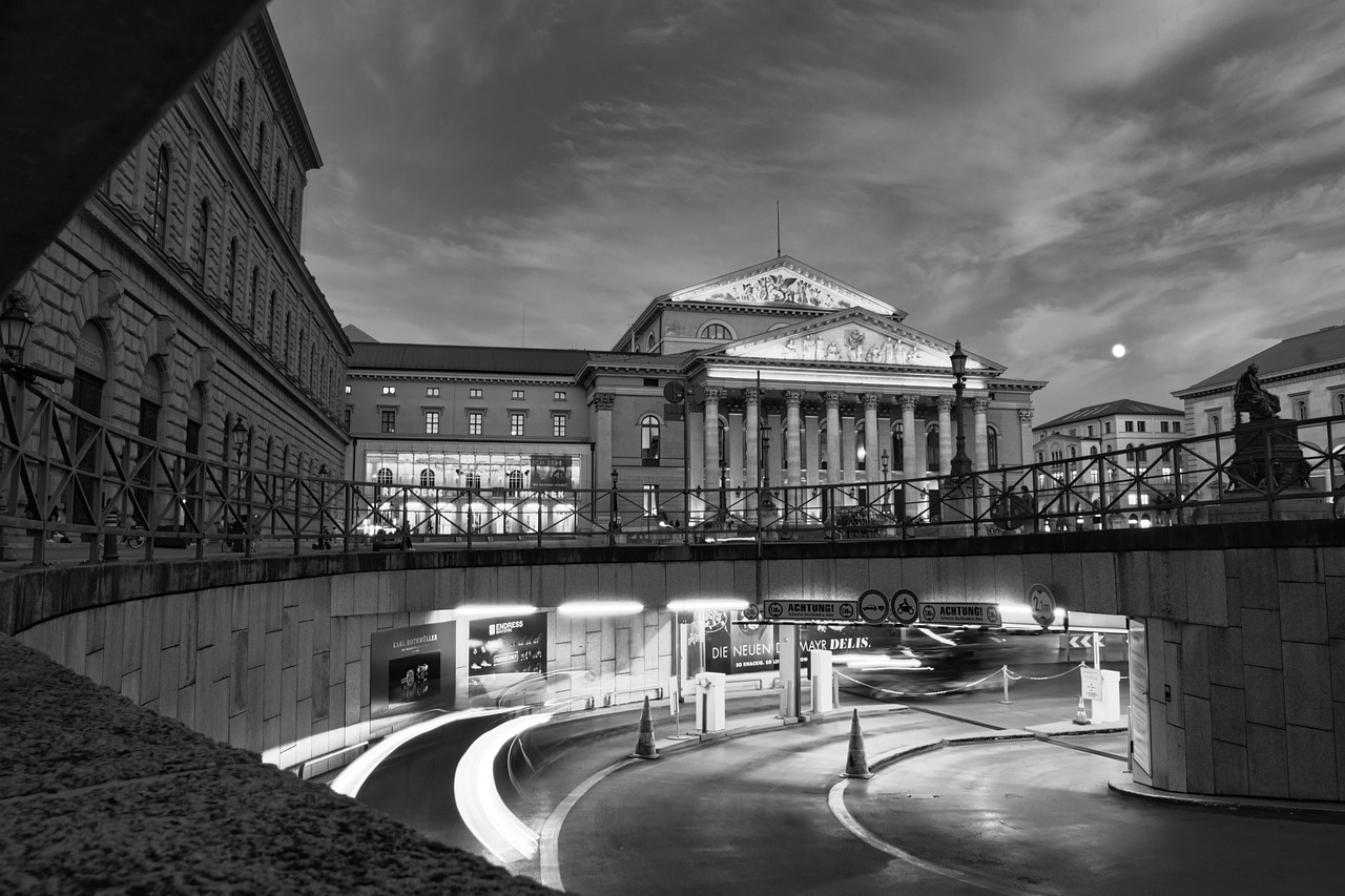 Beleuchtetes Münchner Theatergebäude bei Nacht, Schwarzweißaufnahme mit Mond über der Fassade